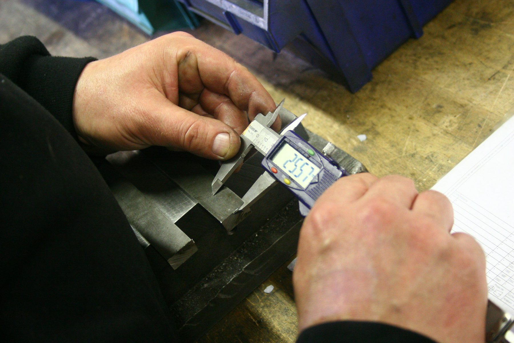 Hands measuring a moulded plastic part with a digital caliper during quality inspection